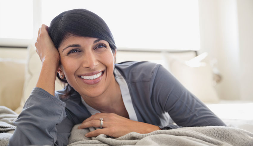 A Close-up of a smiling women lying on a bed with her head propped up by her right hand